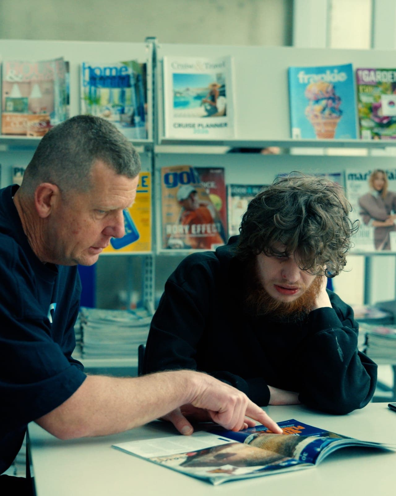 An EmpwrU support worker reading through a magazine with a participant at the library
