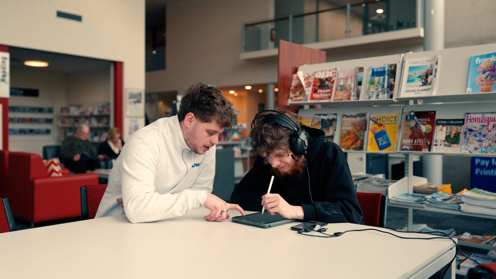 An EmpwrU support worker helping a participant with a drawing tablet at the library