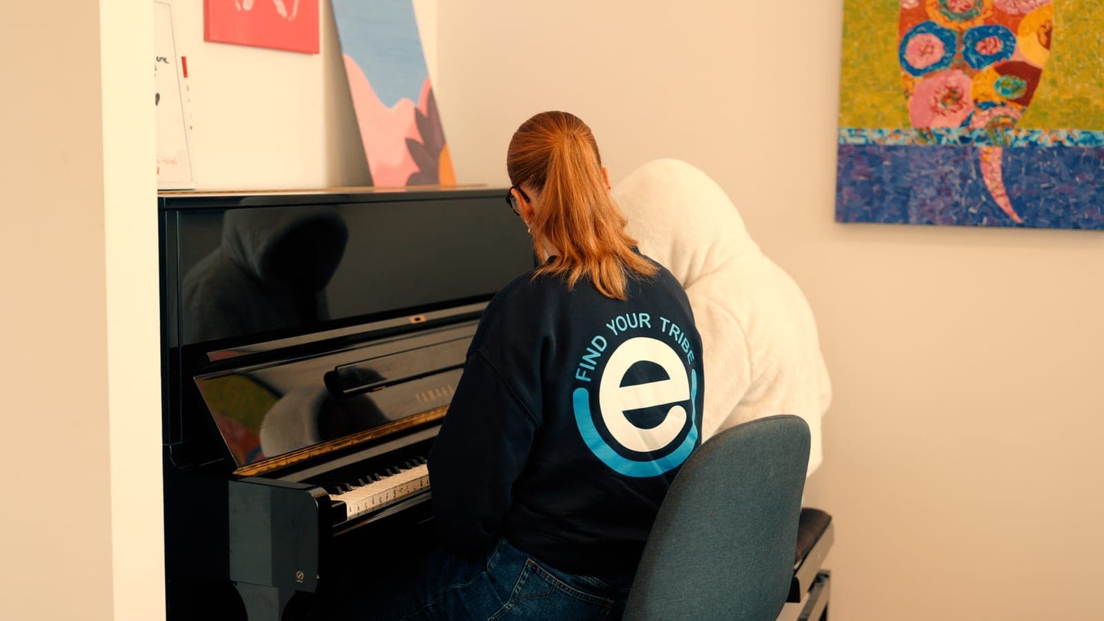 Two people at the piano, one in an EmpwrU Find Your Tribe jumper