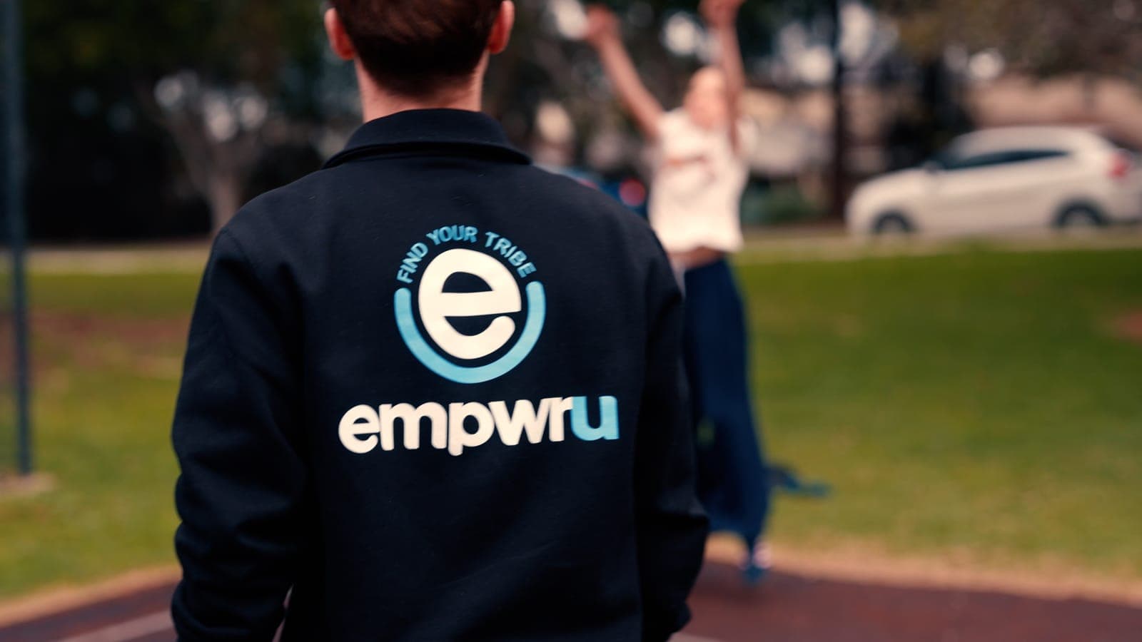 An EmpwrU support worker in a Find Your Tribe jacket at the basketball court